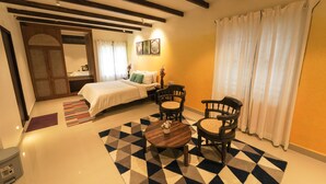 A hotel room with a bed, two chairs, a small table, a rug, and a window with curtains. - Akkandi Veedu (Kodaikanal)