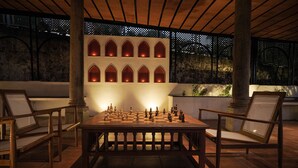 A chessboard set on a wooden table in an outdoor patio area with stone walls and arched niches. - Akkandi Veedu (Kodaikanal)