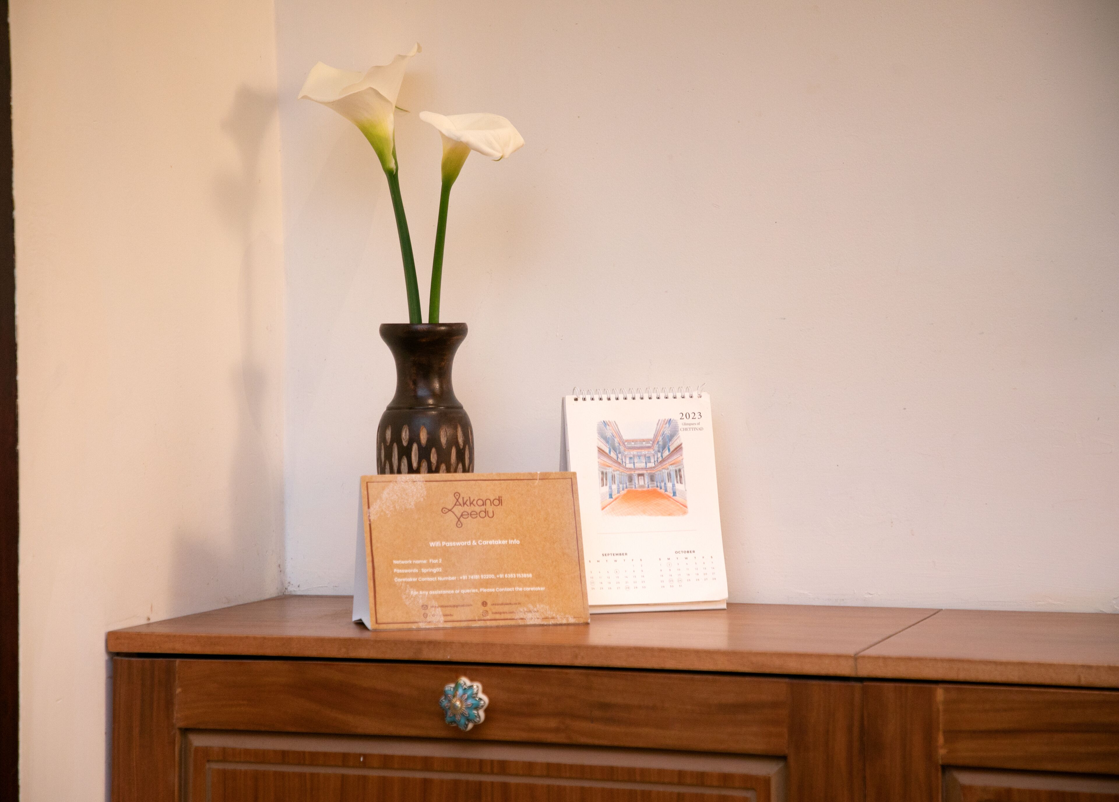 Un aparador de madera con un jarrón de flores blancas y un calendario.