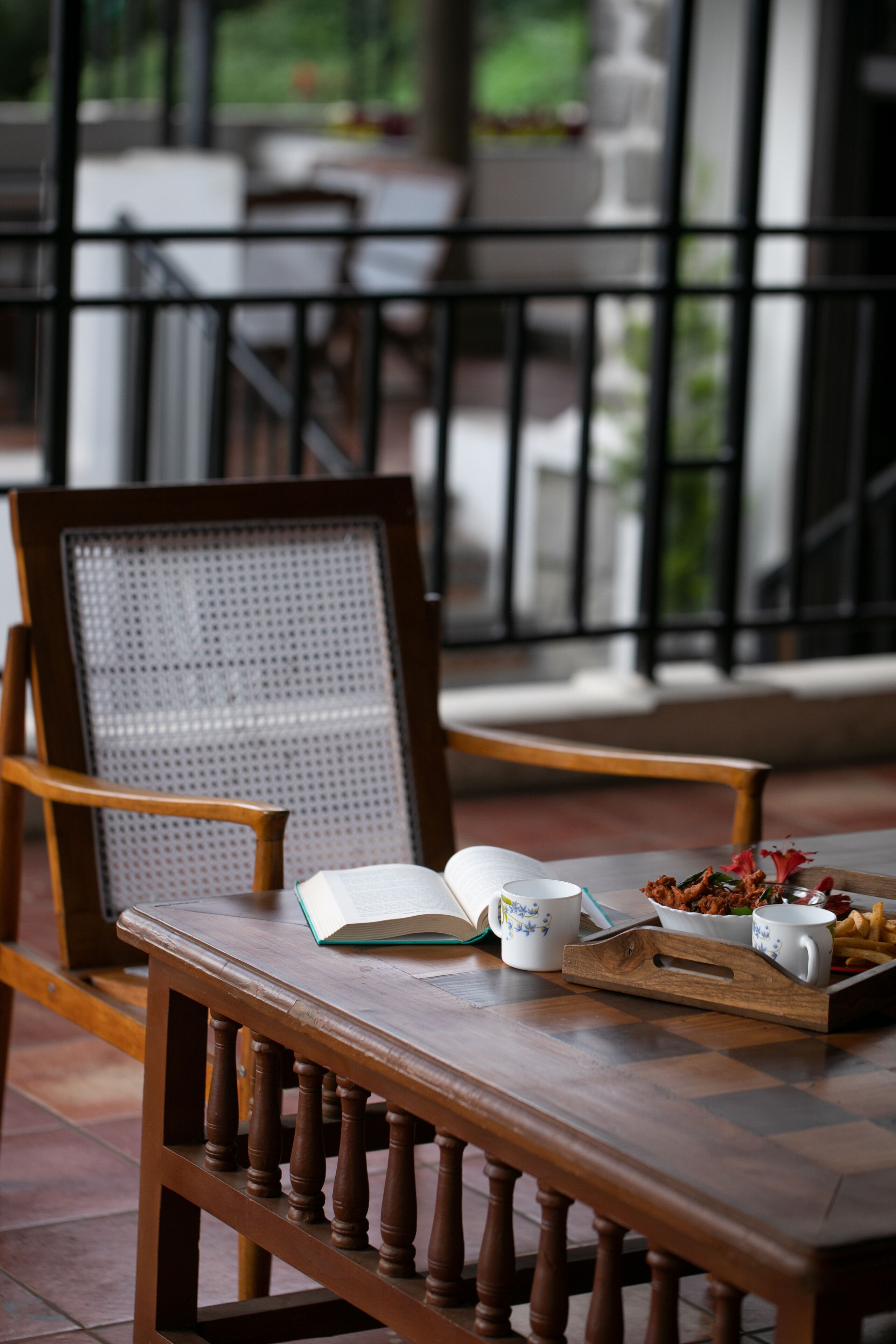 A wooden chair with a woven backrest and a tray table, a book, a mug, and a plate of food on a table.