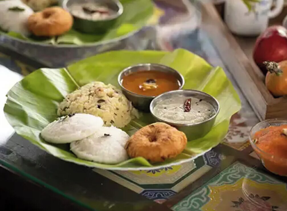 A plate of food with idlis, dosas, and chutneys on a banana leaf.