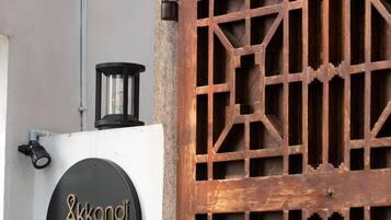 A wooden gate with a geometric pattern, a black circular sign with gold lettering, and a small black lantern on top.