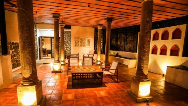 A lobby with a checkered table, chairs, and stone pillars. - Akkandi Veedu (Kodaikanal)