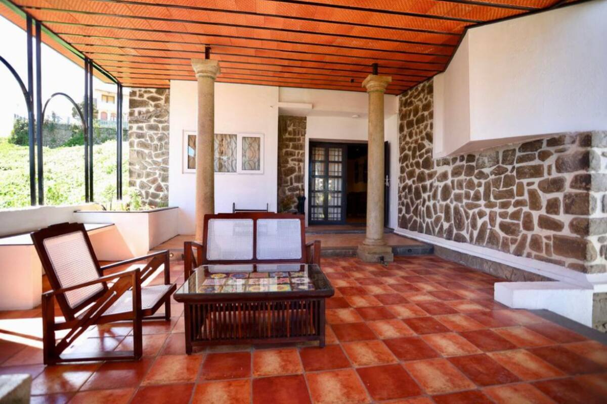 Uma área de varanda coberta com um muro de pedra, um banco de madeira e duas cadeiras.