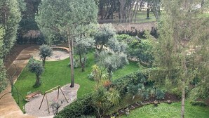 Un jardín ajardinado con diversos árboles, un espacio con bancos de piedra circular y un sendero pavimentado.