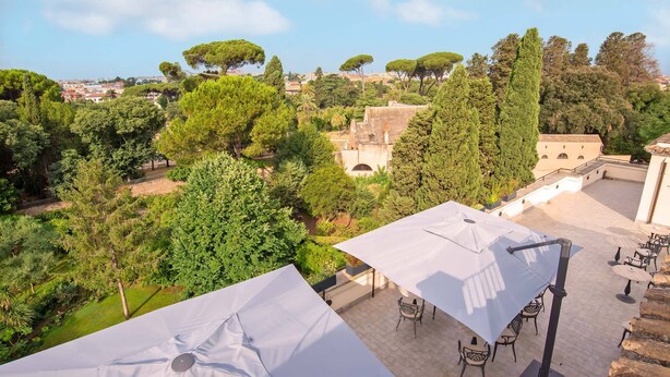 Una terraza al aire libre con sombrillas blancas, sillas y vistas a un pueblo histórico con árboles y edificios.