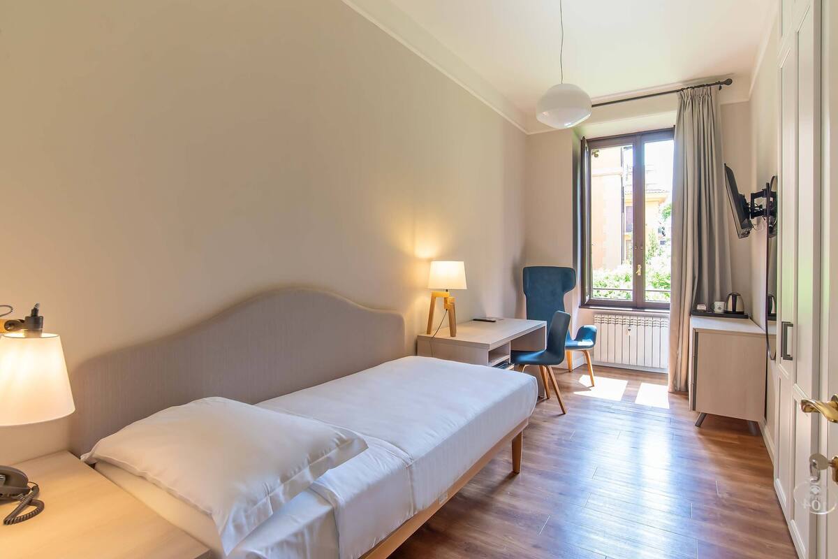 Une chambre d’hôtel avec un lit simple, un bureau, une chaise, une lampe et une vue sur l’extérieur.