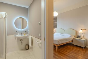 Un bagno moderno con uno specchio rotondo, un lavandino e un water. La stanza ha un pavimento in legno e un letto con un comodino e una lampada.