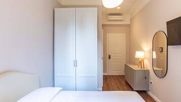 A bedroom with a bed, a wardrobe, a dresser, a mirror, and an air conditioning unit.