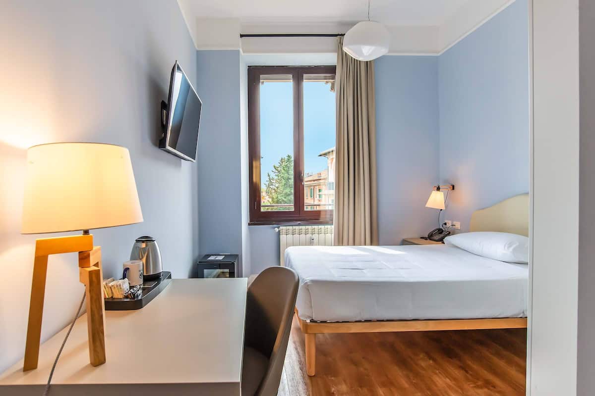 Une chambre d’hôtel avec un lit, un bureau, une chaise, une télévision et une fenêtre avec des rideaux.