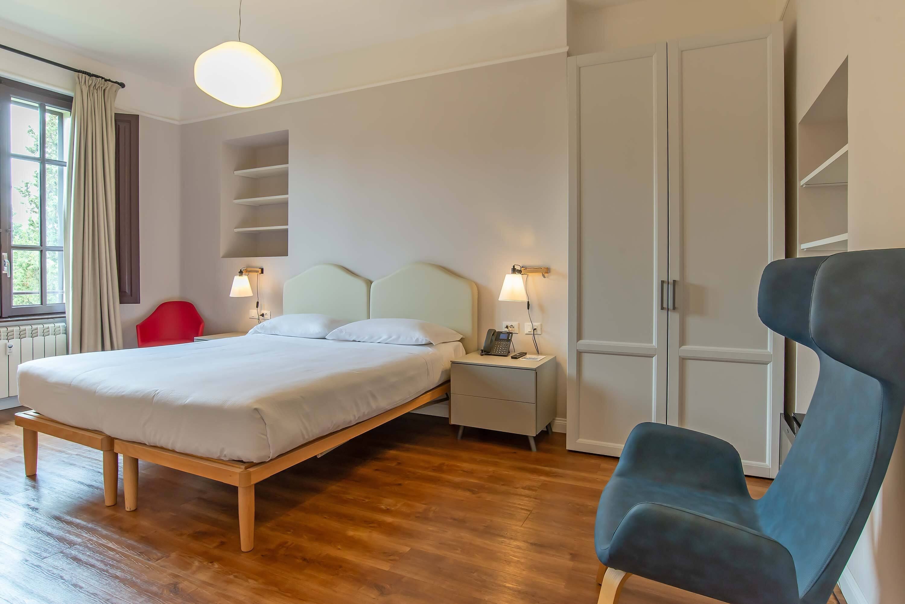 Ein Schlafzimmer mit einem Bett, Nachttischen, einem Sessel und einem Kleiderschrank.