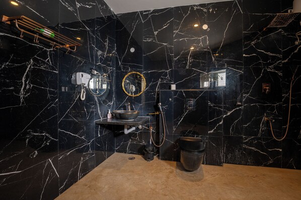 A modern bathroom with black marble walls, a beige countertop, a sink, a mirror, a handheld showerhead, and a toilet.
