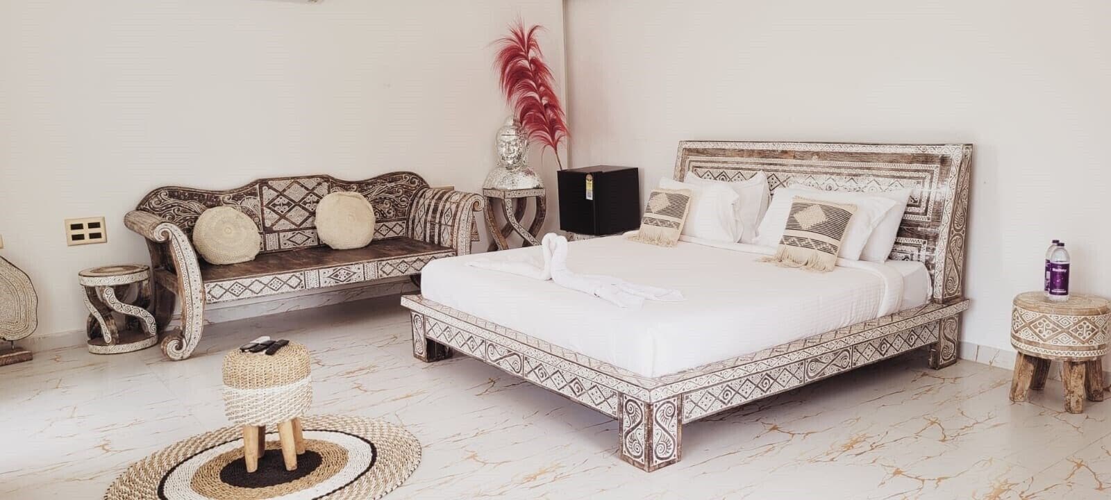 A bedroom with a large bed, a sofa, a small table, and decorative items.