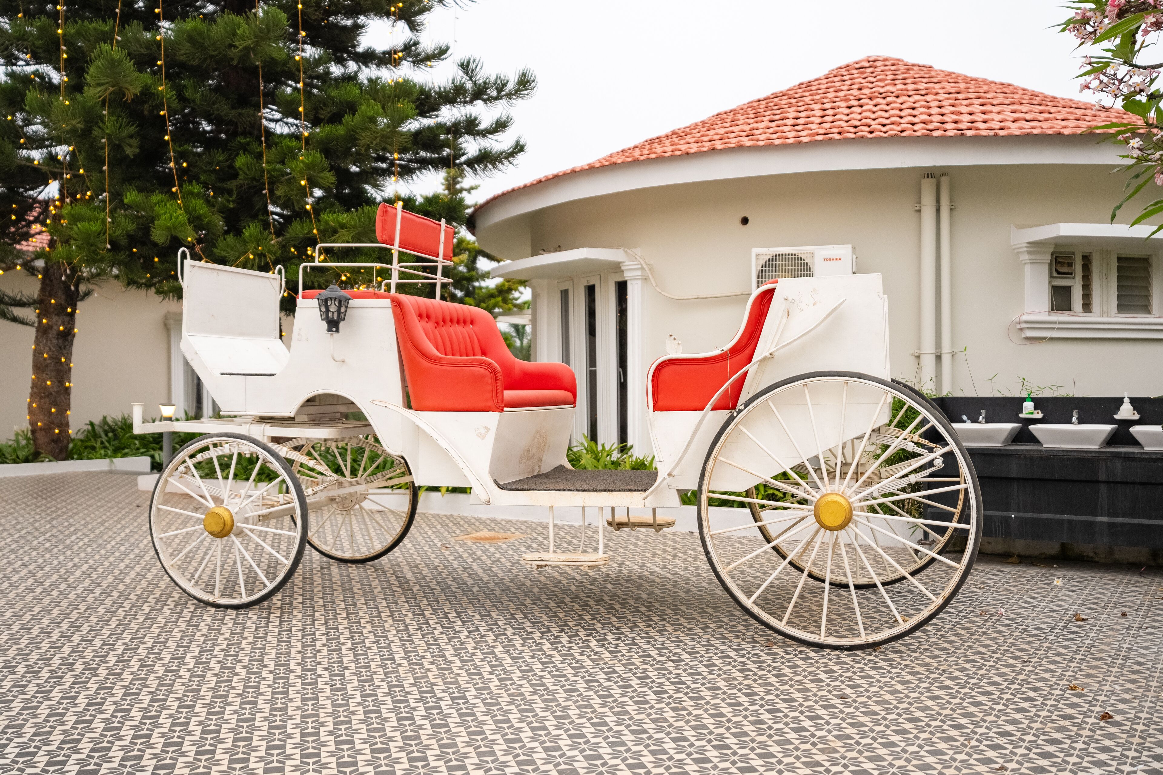 A white horse-drawn carriage with red seats parked on a tiled surface.