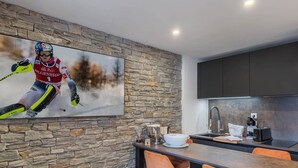 Uma cozinha moderna com parede de pedra, uma grande pintura de um esquiador e um espaço bar com cadeiras laranja.