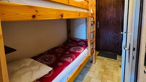 Ein Schlafraum mit Etagenbetten, einer Holzlade, einer Tür und einer gemusterten Bettdecke.