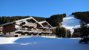 Ein mehrstöckiges Chalet mit Balkonen vor einer verschneiten Berglandschaft.