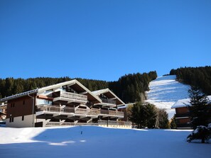 A multi-story chalet with balconies, set against a snowy mountain backdrop. - Cozy studio for 4 pers with south-facing balcony (Les Saisies)
