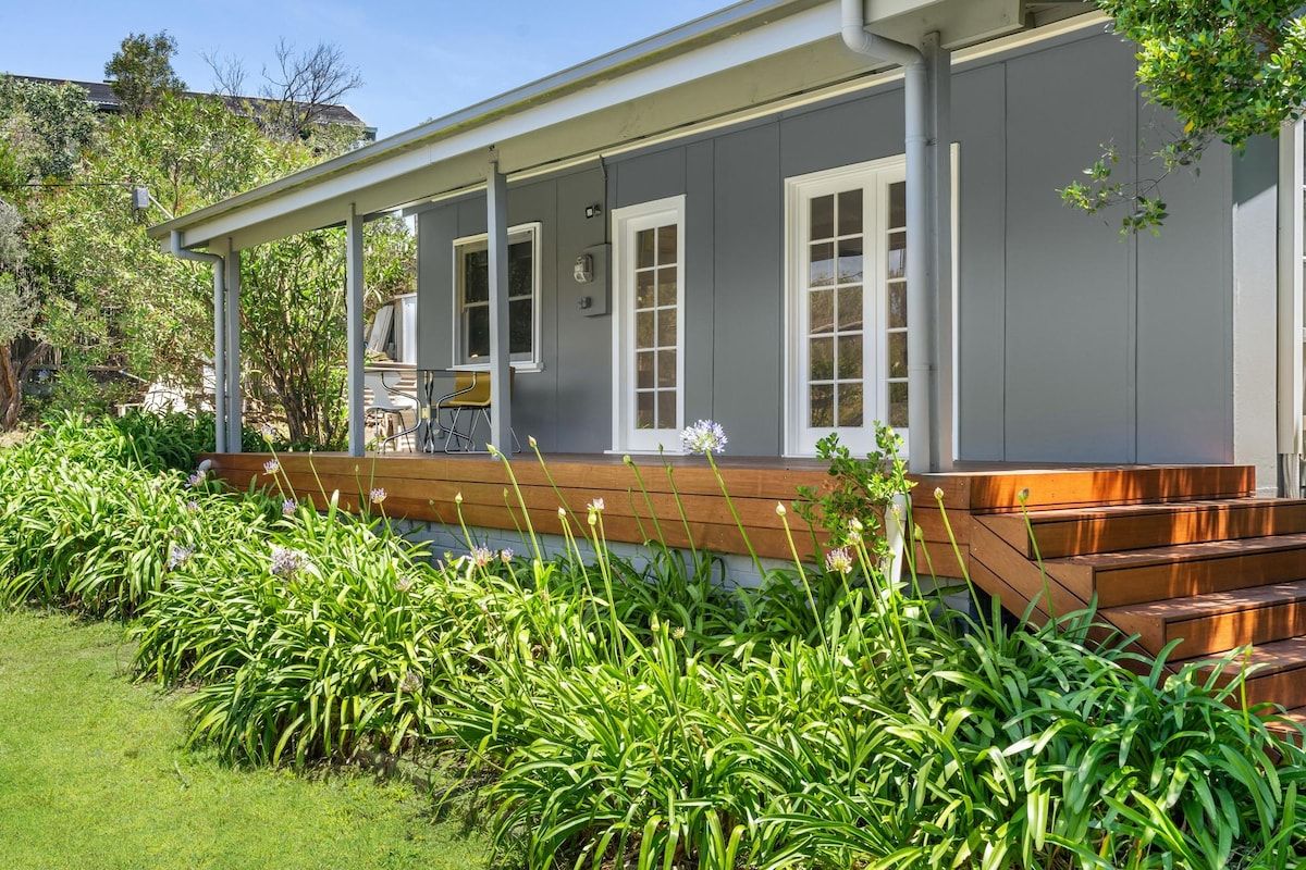 A house with a covered porch, a wooden deck, and a garden with green plants and flowers.