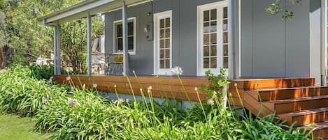 A house with a covered porch, a wooden deck, and a garden with green plants and flowers.
