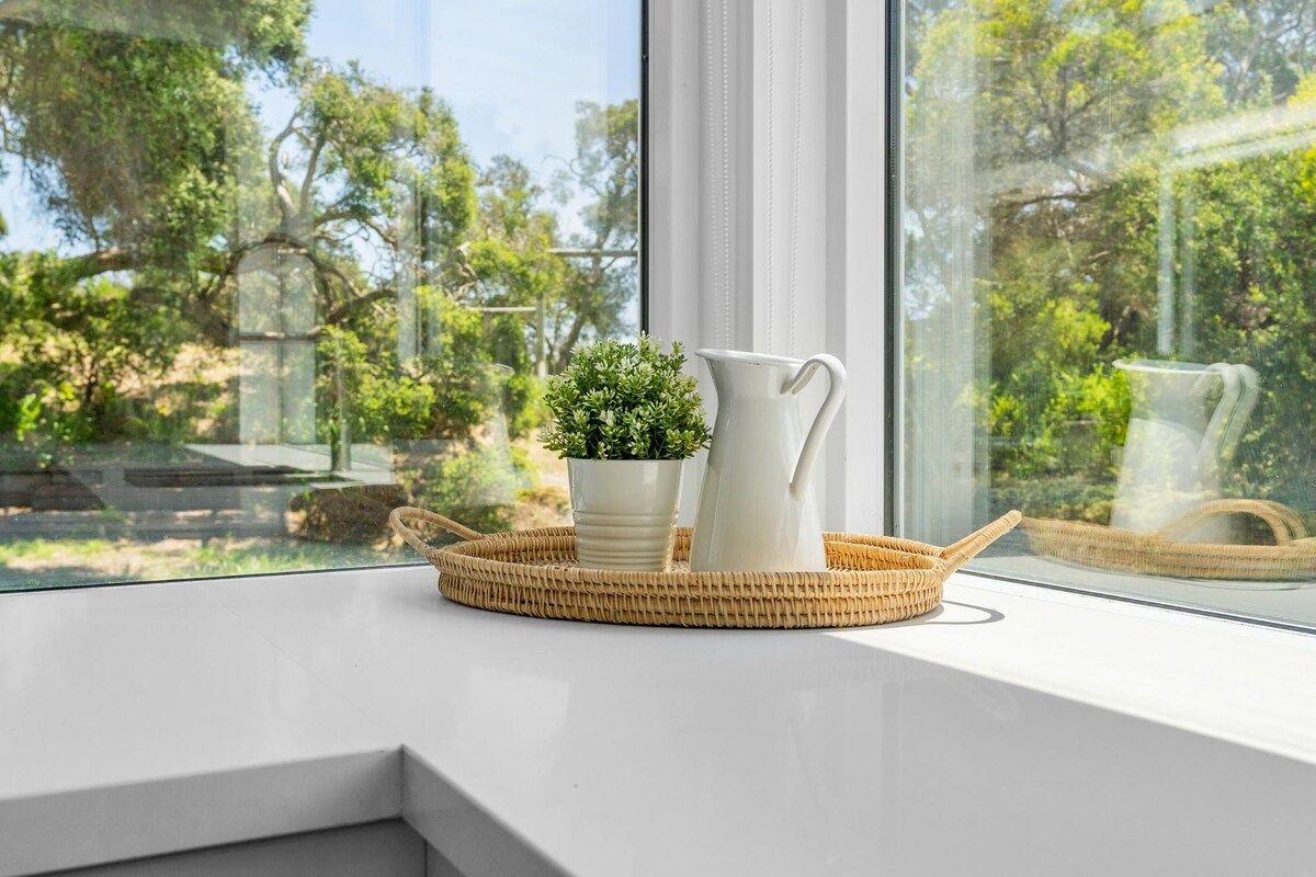 Una ventana con una cesta tejida que contiene una planta en maceta y una jarra blanca sobre un alféizar blanco.
