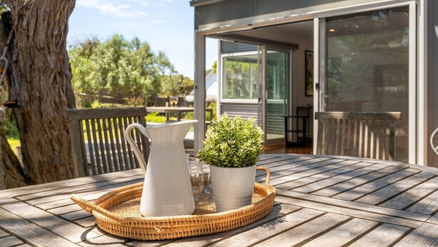 A wooden table with a white pitcher and a potted plant on a wicker tray.