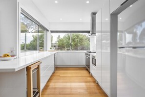 Een moderne keuken met witte kasten, een houten vloer en een groot raam met uitzicht op bomen.