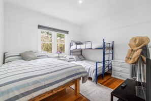 Een slaapkamer met een eenpersoonsbed, een stapelbed, een bureau, een stoel, een televisie en een raam met uitzicht op bomen.