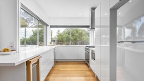 A modern kitchen with white cabinets, a wooden countertop, and a view of trees through large windows.