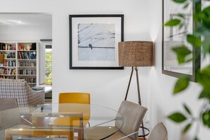 A modern living room with a glass coffee table, a yellow chair, a sofa, a bookshelf, and a framed picture on the wall.