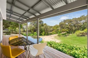 An outdoor patio with a glass table and chairs, surrounded by greenery and a view of the landscape.