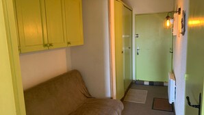 En smal hall med en brun soffa, en grön dörr och en väggmonterad lampa.