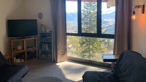 Ett vardagsrum med en tv, en bokhylla och ett stort fönster med utsikt över bergen.