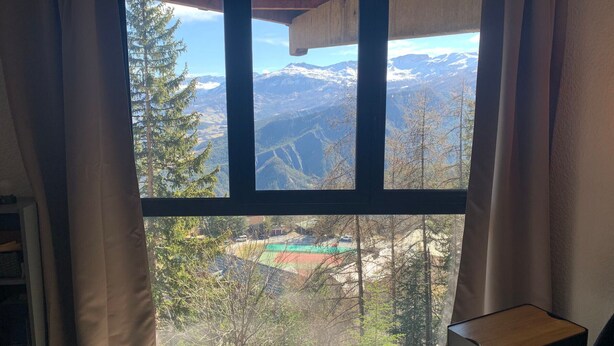 Ett rum med ett stort fönster som ger utsikt över bergen, ett litet bord och en bokhylla.