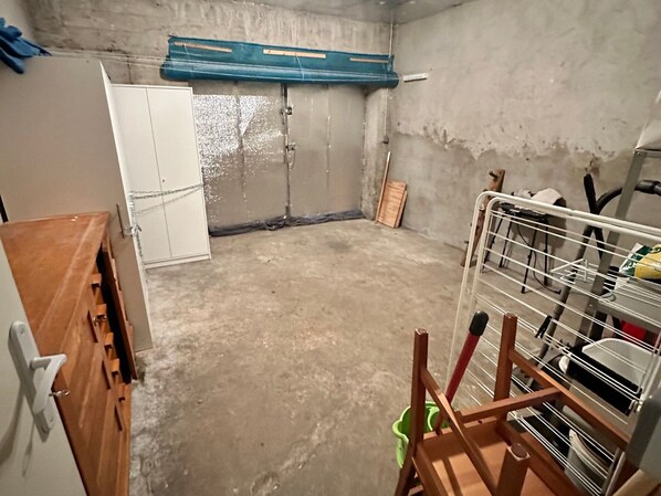 A room with a concrete floor, a white wardrobe, a blue door, and a metal rack with shelves.