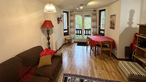 Un salon confortable avec un canapé, une table et une lampe. On peut admirer un jardin à travers une porte vitrée.