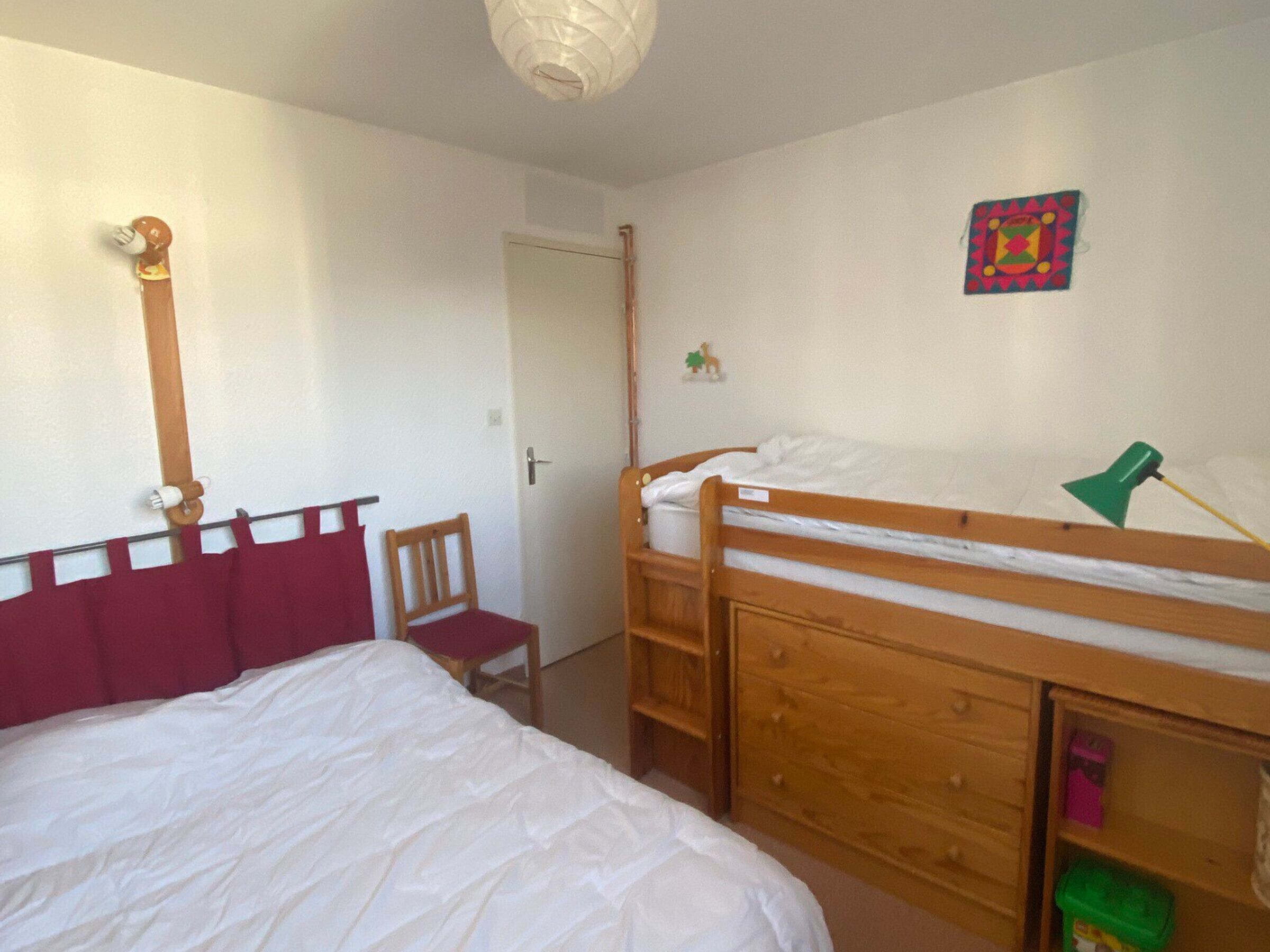 Quarto com uma cama beliche, uma cadeira, um armário de madeira e uma porta.