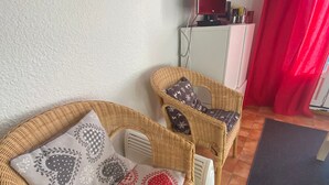 A wicker sofa with patterned cushions, a white cabinet, and a red curtain in a room with tiled flooring.