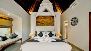 Een hotelkamer met een groot bed, een houten bankje, een bakstenen muur en een plafond met een houten balk.