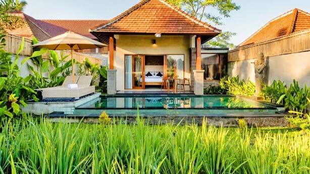 Een villa met een zwembad, een overdekt terras en weelderige begroeiing.
