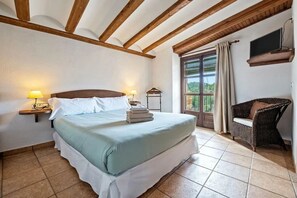 Une chambre à coucher comprenant un lit, des lampes de chevet, une fenêtre avec des rideaux, une chaise et un téléviseur fixé au mur.
