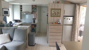 A compact living space with a kitchenette, a dining area, and a sofa. - Mobil-home Dans Petit Camping Tranquil. Calme, Ombragé et Nombreuses Activités (Orgnac-l'Aven)