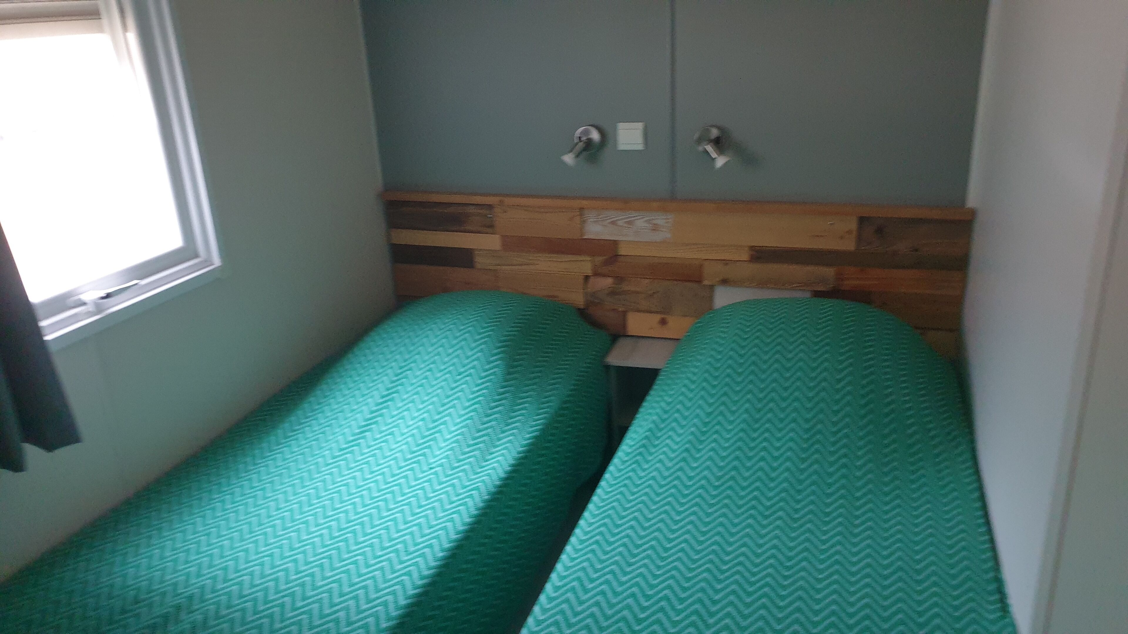 A small room with two single beds, a wooden headboard, a window, and a door.