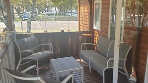A covered porch with a seating area, including a table and chairs, and a view of parked cars and trees in the background. - Mobil-home Dans Petit Camping Tranquil. Calme, Ombragé et Nombreuses Activités (Orgnac-l'Aven)