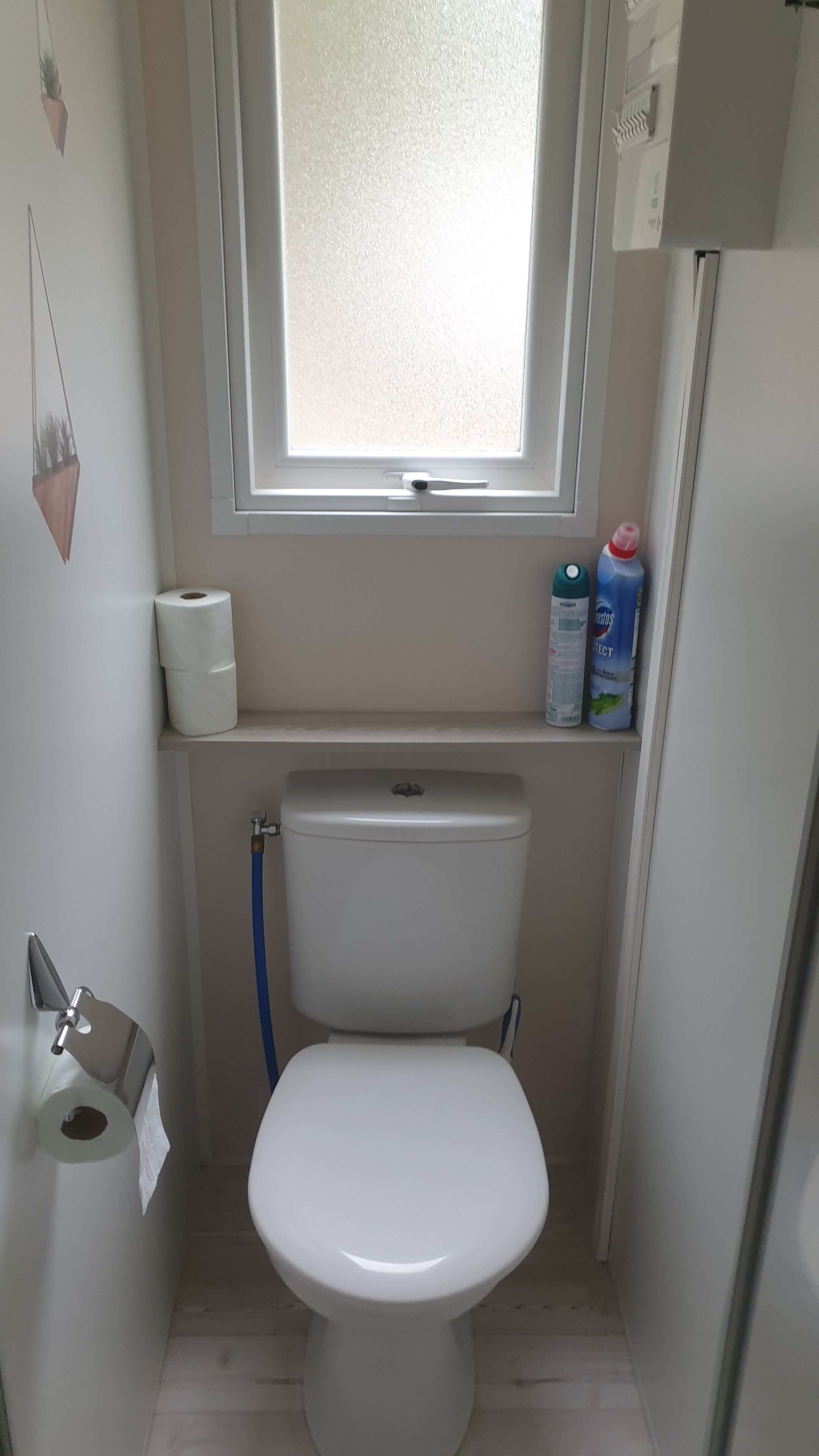 Une petite salle de bain propre, équipée de toilettes, d’une fenêtre et d’une étagère où sont rangés les articles de toilette.