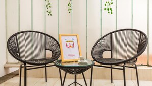 Two black wicker chairs around a small glass table with a framed picture and a cup.
