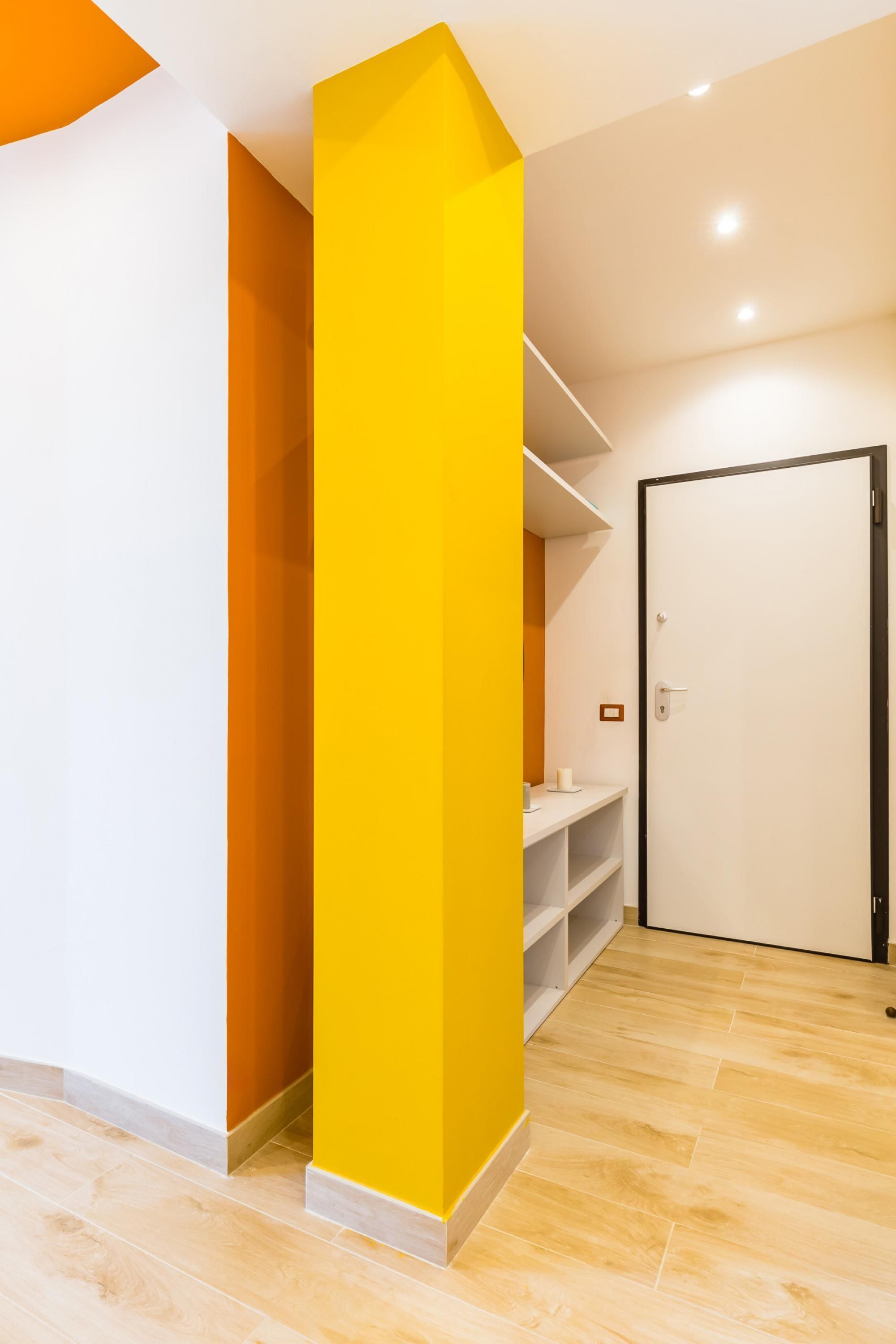 Un interior moderno con un pilar amarillo brillante, paredes blancas y suelo de madera.