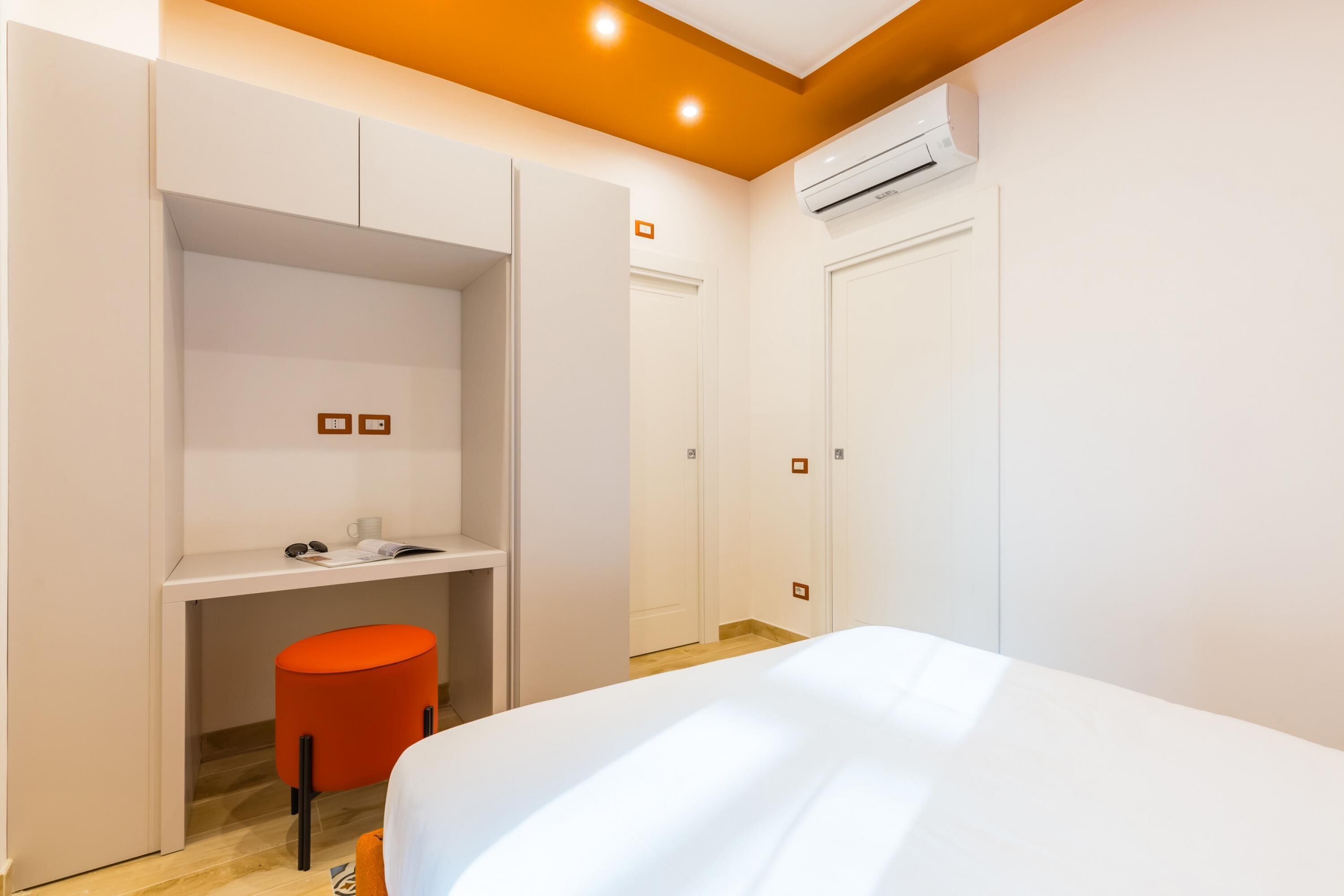 Een slaapkamer met een bed, een bureau en een stoel. Er is een airconditioner aan de muur bevestigd.