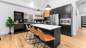 A modern kitchen with a central island, bar stools, a coffee bar, and a refrigerator. - Your Relaxation Destination at Emerald Shores (Hollister)