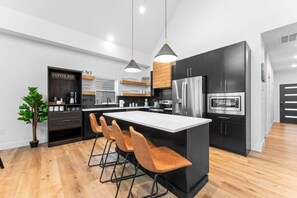 A modern kitchen with a central island, bar stools, a coffee bar, and a refrigerator. - Your Relaxation Destination at Emerald Shores (Hollister)